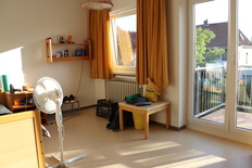 Bild zeigt ein Bewohnerzimmer im Selbstständigenhaus. Zu sehen ist ein Fenster und der Zugang zum Balkon.