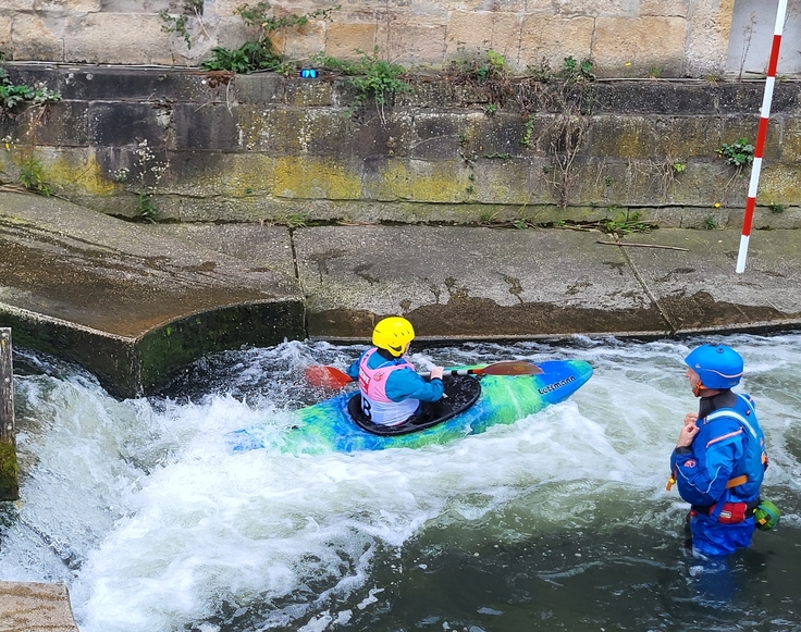 Auf diesem Bild zu sehen sind bunte Kanus und Kanuten, beim Einstieg in das Kanu an der Kanustrecke auf der Innerste in Hildesheim, bei der Abfahrt auf der Welle.