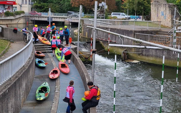 Auf diesem Bild zu sehen sind bunte Kanus und Kanuten, beim Einstieg in das Kanu an der Kanustrecke auf der Innerste in Hildesheim, bei der Abfahrt auf der Welle.
