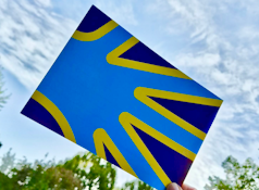 Auf dem Bild ist eine dunkelblaue Karte mit einer stilisierten Hand in hellblau mit gelbem Rand zu sehen. Das sind die Farben Flagge der Gehörlosen.